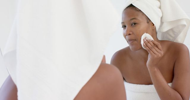 Woman with towel on head cleaning face with cotton pad in bathroom - Download Free Stock Images Pikwizard.com