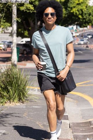 African american man walking city street with coffee and crossbody bag wearing sunglasses