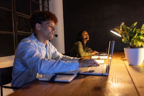 Night shift customer support team collaborating on laptops with headsets in modern office