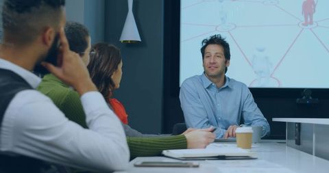 Presenting man explaining network diagram to colleagues in modern boardroom meeting