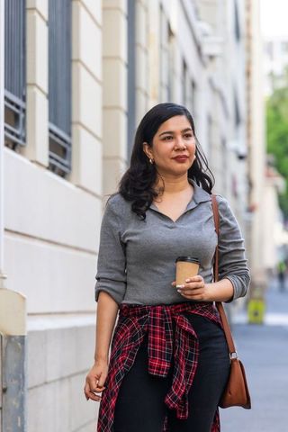 Urban commuter walking with coffee and satchel, casual sweater and plaid tied at waist