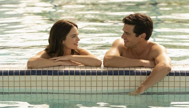 Smiling couple relaxing at resort pool edge, romantic summer getaway, sunny swimwear