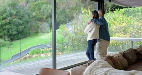 Diverse couple standing by floor-to-ceiling glass overlooking lush garden and deck