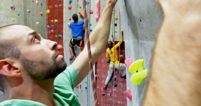 Individuals engaged in rock climbing at an indoor climbing gym. The image shows one person in the foreground focusing on their next move while two more climbers in the background make their way up the climbing wall. This image can be used to promote fitness activities, adventure sports, and healthy lifestyle choices. Ideal for gym advertisements, sports equipment catalogs, fitness blogs, and social media content related to exercise and climbing.