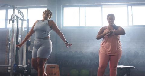 Plus-size black women working out together in backlit gym with fitness trackers