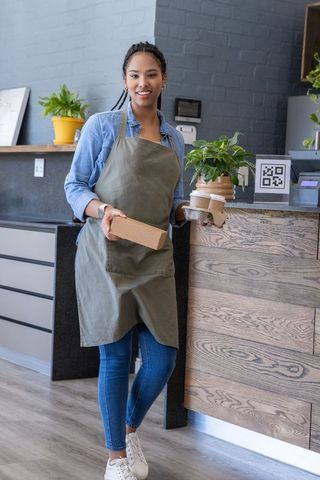 African american barista serving takeaway coffee and box at modern cafe counter with qr