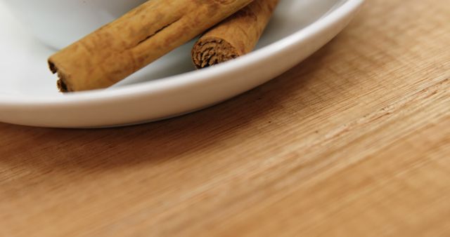Cinnamon sticks rest on a white saucer placed on a wooden surface, with copy space. Their warm, earthy tones suggest a setting related to cooking or baking.