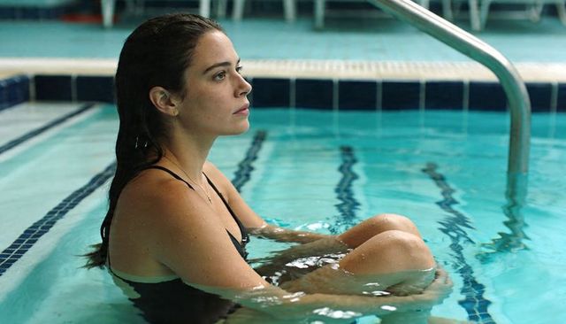 Woman sitting in indoor pool holding knees, contemplating wellness and solitude