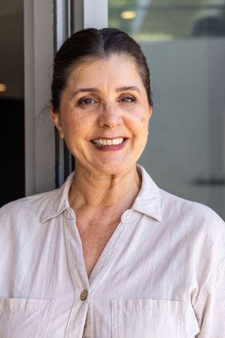 Senior woman smiling in doorway wearing beige collared shirt, natural light portrait