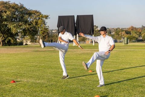Diverse team athletes performing dynamic kicking warmup drills on sunny grassy field with cones