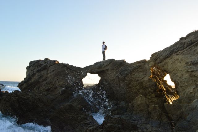 Person Standing on Rocky Outcrop by Ocean Waves at Sunset - Download Free Stock Photos Pikwizard.com