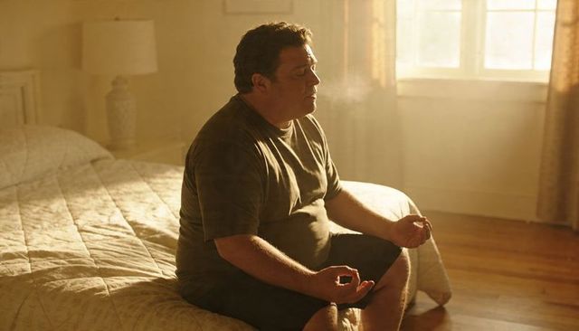 Middle-aged man meditating on bed in sunlit bedroom morning light, mindfulness and calm