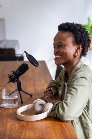 African american woman smiling while recording podcast with microphone and headphones