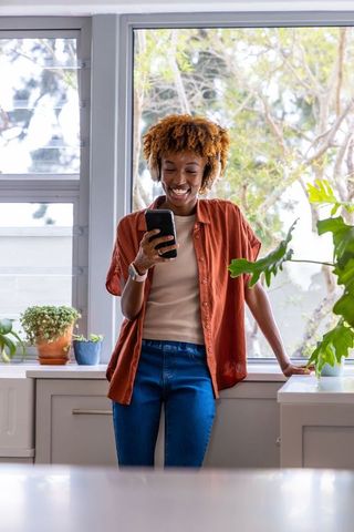 African american woman leaning on kitchen counter using smartphone and headphones