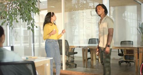 Diverse coworkers collaborating and brainstorming at glass-walled meeting space with marker