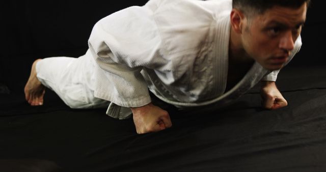 Man wearing martial arts uniform practicing push-ups on knuckles, showcasing strength and determination. Suitable for use in fitness, martial arts training promotions, endurance exercises, strength training materials, and showcasing disciplined workout routines.