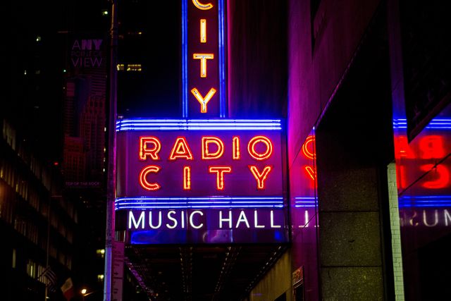 Vibrant neon sign of Radio City Music Hall glowing in the night captures the essence of New York City's nightlife and iconic landmarks. Perfect for promoting tourism, urban life blogs, travel guides, concert listings, entertainment announcements, or brand advertisements related to music and performance venues.