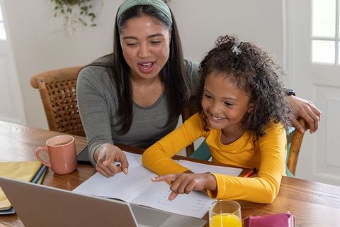 Multiracial mother and daughter studying together at kitchen table, online tutoring moment