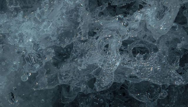 Glassy ice macro texture revealing bubbles, crystal threads and frosty facets