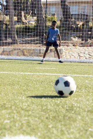 African american teen goalkeeper guarding goal on sunny turf watching soccer ball ready