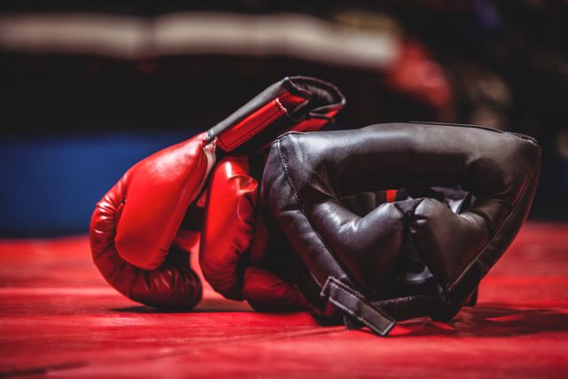 Boxing gloves and headgear lying on a boxing ring floor. Ideal for use in sports and fitness articles, boxing training promotions, gym advertisements, and martial arts equipment catalogs.