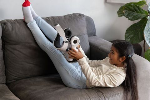Girl reclining on gray sofa holding futuristic robot toy, enjoying playful indoor moment