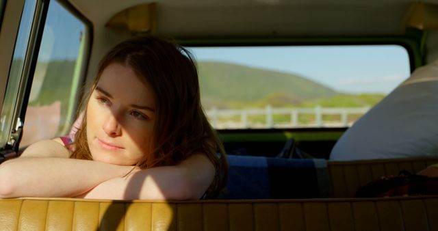 Young woman leaning on car seat, enjoying moment during road trip in countryside. Ideal for travel blogs, promotional materials for road trip adventures, ads for car rentals, or lifestyle magazines featuring travel and leisure.