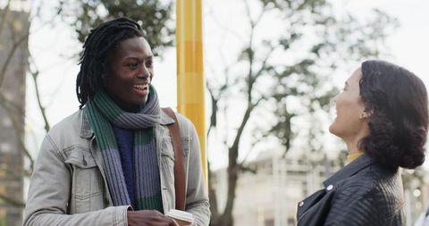 Diverse friends chatting on city sidewalk, holding coffee, wearing scarves and jackets