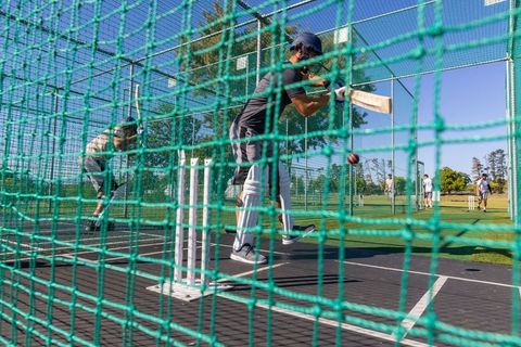 Cricket batter practicing in outdoor nets wearing helmet and pads during sunny training