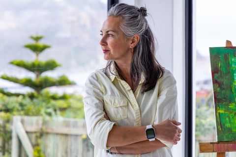 Mature artist gazing out of studio window wearing smartwatch with green canvas on easel