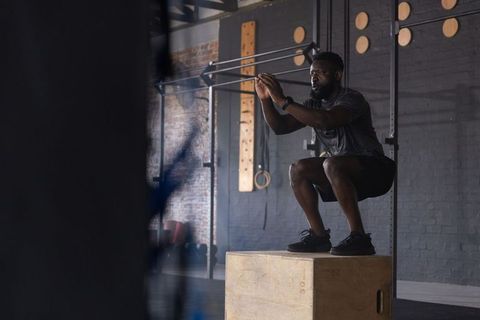 African american athlete performing box squat on plyo box in industrial gym