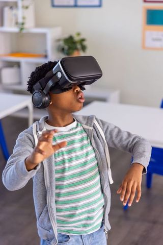 African american boy exploring virtual reality in classroom wearing vr headset and headphones