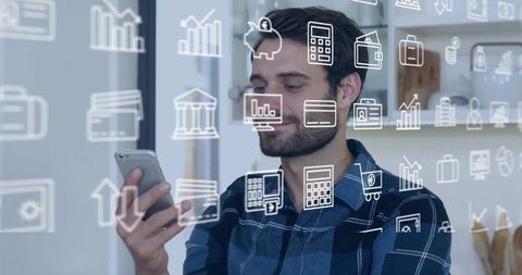 Man holding smartphone viewing finance and business app icons on glass in modern workspace