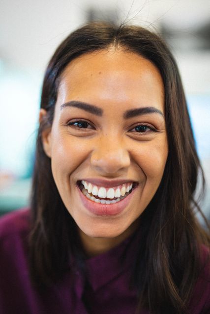 This image captures a close-up of a smiling young biracial businesswoman in a creative office environment. Ideal for use in corporate websites, business presentations, marketing materials, and articles focusing on diversity, workplace culture, and professional success.