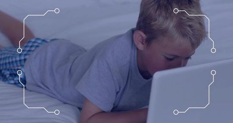 Young boy lying on bed focusing on laptop with tech circuit overlay for e-learning
