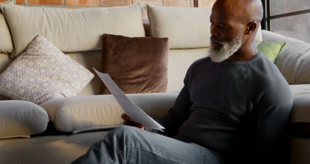 African American man reviews documents at home, with copy space. He sits comfortably on a couch, immersed in reading the paperwork.