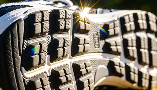 Close-up athletic shoe sole with deep tread, sun flare, rainbow starburst, outdoor