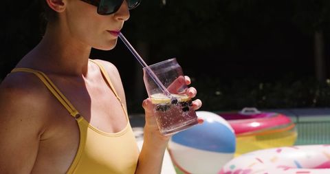 Woman Enjoying Refreshing Drink by Pool with Inflatables