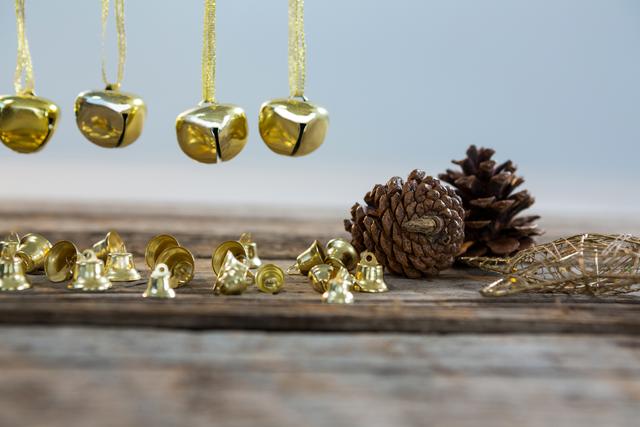 This festive arrangement features golden Christmas bells and pine cones on a wooden table, evoking a warm, rustic holiday feeling. Ideal for use in holiday greeting cards, festive season promotions, and winter-themed advertisements.
