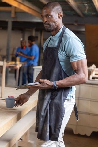 African american carpenter using tablet and sipping coffee working in rustic woodshop