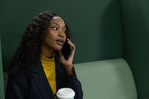 African american professional woman talking on phone in green private booth holding coffee