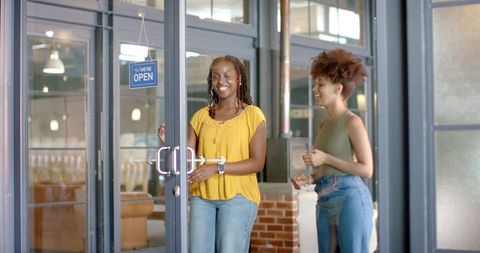 Two african american women entering cafe through glass doors, smiling and greeting