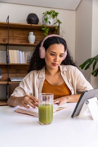 African american woman studying with tablet and green smoothie, wearing pink headphones