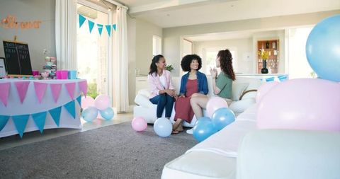 Friends celebrating baby shower at home with pastel balloons, bunting and cupcakes