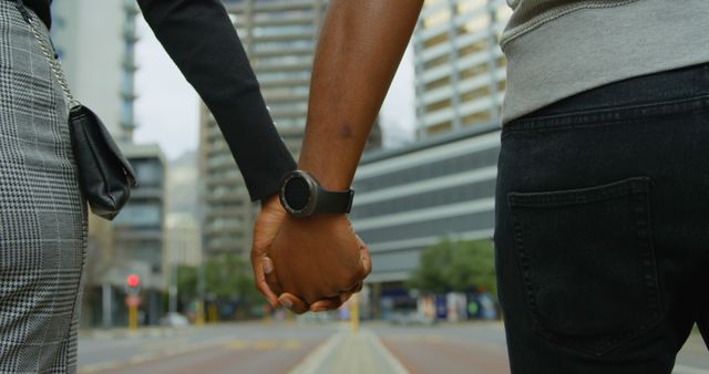 Close-up rear view of joyful couple holding hand while walking in city street. Man wearing smartwatch, in slow motion.