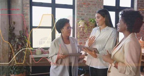 Three colleagues discussing tablet data with overlaid charts during loft office team review