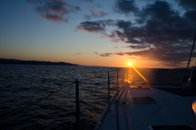 Captivating image of a serene sunset viewed from the deck of a sailboat on a calm ocean. Perfect for travel blogs, adventure themes, nature photography collections, and maritime promotions. Evokes feelings of peace, tranquility, and wanderlust.
