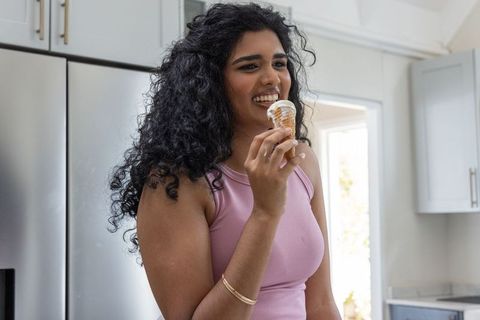 Smiling indian woman enjoying soft-serve ice cream in modern kitchen