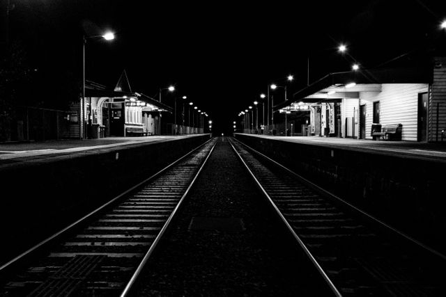 Dark, empty train station at night with illuminated platforms. Ideal for conveying themes of solitude, isolation, travel, urban scene, or night-time city life. The symmetrical composition and contrast enhance drama and serenity, perfect for backgrounds, blogs, or travel-related content.