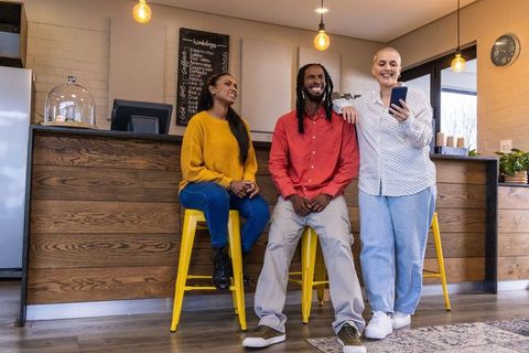 Diverse friends chatting and laughing at modern coffee counter with yellow stools